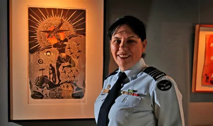 Wing Commander Cheryl Neal dressed in her air force uniform is standing in front of Indigenous artwork.