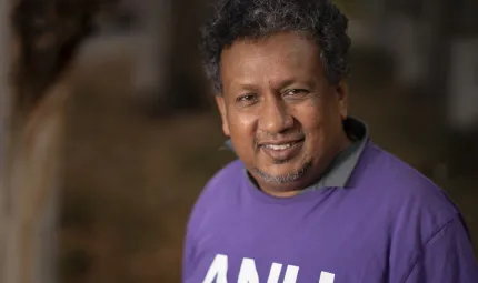 Aboriginal man with curly dark hair wearing a purple top with the letters A.N.U. on the front.