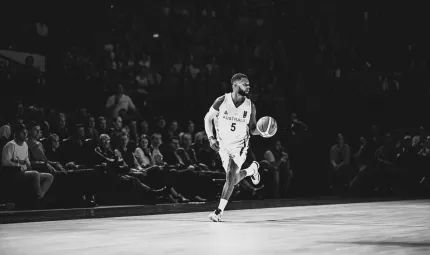 Indigenous man in the Australian basketball uniform dribbles a basketball down the court with a crowd in the background looking on.