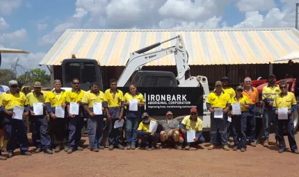 A group of men and women holding certificates while standing in front of heavy machinery and a shed.