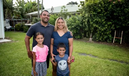 A family photo with a father, mother daughter and son standing in their backyard.