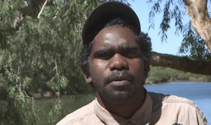 Aboriginal young man dressed in ranger uniform in foreground with river and trees in the background.