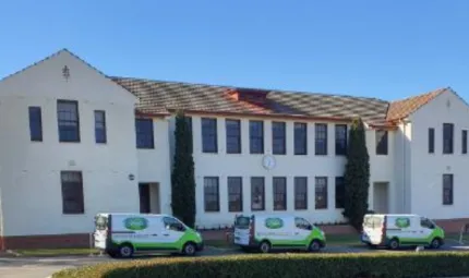 Three white and green vans line up on the roadway in front of a large white building with lots of windows and a red tile roof.