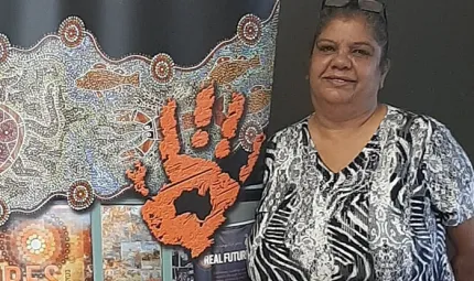 At left is a traditional design featured the imprint of a hand and below are some publications. At right is a woman with glasses on her head and she wears a black and white dress with Aboriginal designs.