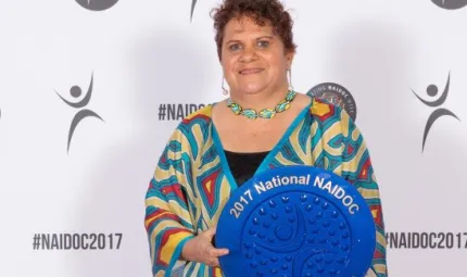 An Aboriginal woman in a colourful top holds a large blue plate.