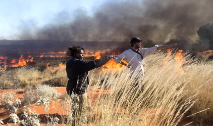 Female ranger and male ranger standing in desert setting with burning grass in the background.