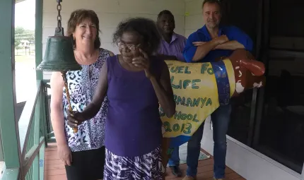 An Indigenous woman ringing a bell in foreground with three people behind her.