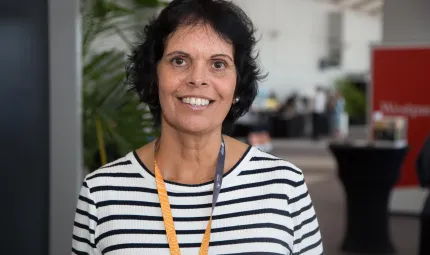 Indigenous woman with dark hair and white shirt with thin navy stripes smiling at Darwin Indigenous Trade Fair.