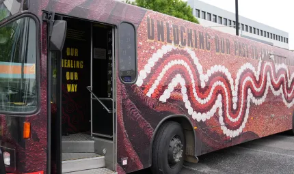 Image of a bus parked outside an office. It is painted with an Indigenous style design.