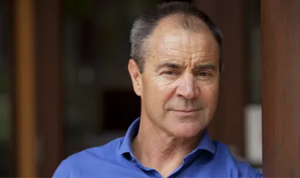 A man in a blue business shirt leans against a vertical timber support beam. He is smiling.