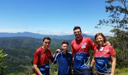 Three men and one woman wearing red and blue short sleeve shirts standing outside with mountain ranges in background.