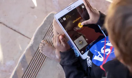 A child using the app on an iPad. The screen shows a word in language, with interactive buttons for learning.