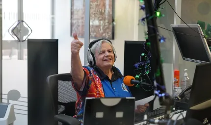 Broadcaster Lorraine Rogers in the recording studio. She is looking at the camera giving the thumbs up.