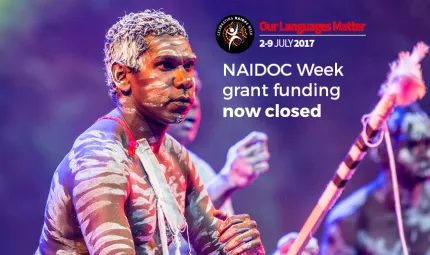 Three Indigenous men covered in traditional paint doing a traditional dance. The following words are shown: NAIDOC Week grant funding now closed.