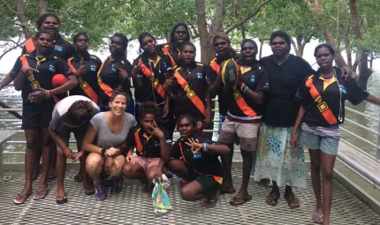 A group of young Indigenous women and their female supervisor standing near a body of water and trees.