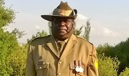 Aboriginal man in full army uniform standing with trees in the background.