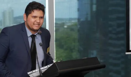 A young Aboriginal man wearing a suit and tie is speaking at a rostrum.