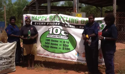 Four women rangers standing next to large green and white banner which says, happy recycling day.