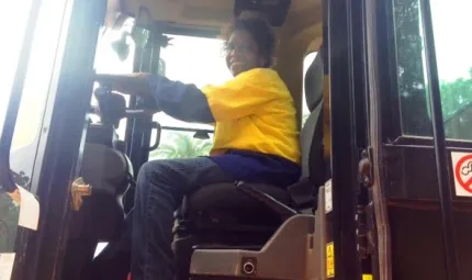 Indigenous woman - Sandra Gillman - sits in the cab of a front end loader wearing yellow and blue safety clothing.