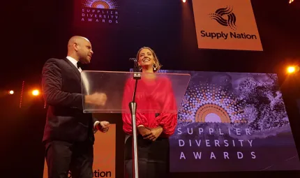 A man and a women stand at a lectern. Behind them is a sign with the Supply Nation logo and another sign with the text Supplier Diversity Awards.