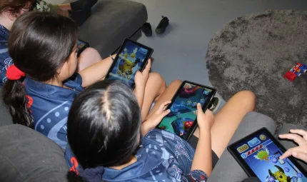 A group of children in blue school uniforms holding tablets, playing a game.