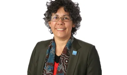 Aboriginal woman wearing glasses, a dark jacket and scarf covered with Indigenous designs.