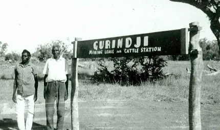 Black and white photo showing strikers Vincent Lingiari and Mick Rangiari in front of a sign that says 'Gurindji Mining Lease and Cattle Station'.