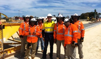 A group of seven men at a construction site, wearing high-vis vests and hard hats.