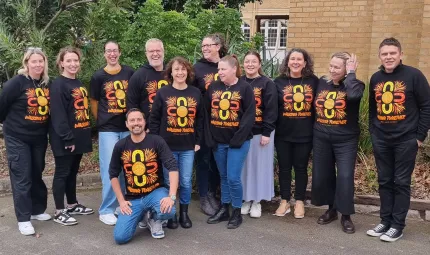 A group of smiling people wearing shirts with a matching brightly coloured design and the text 'Walking Together'