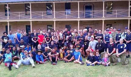 Large group of Indigenous youth and young adults and police officers sit and stand on a lawn in front of a two-storey building.