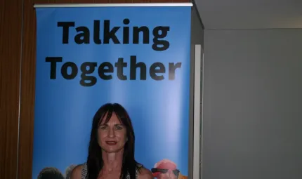 Woman standing in front of poster with displayed words, Talking Together