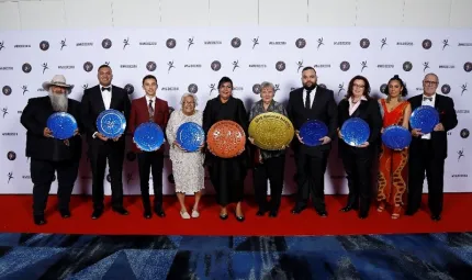 12 award winners stand in a row with a logo photo wall behind, on the NAIDOC 2018 red carpet