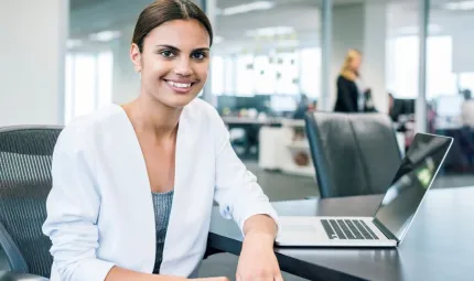 Female businesswoman smiling to camera sitting at desk with laptop open