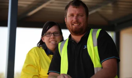 Woman in yellow shirt standing to left and behind man in dark shirt with safety vest.