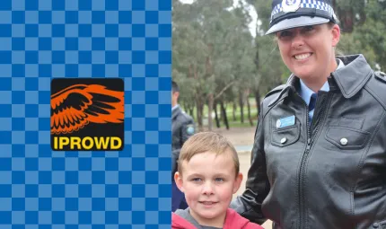 On the left, orange wings on black background with letters IPROWD beneath them all on light and dark blue checked background. On the right, a young boy in red and grey coat stands next to woman in police uniform.