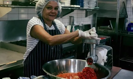 Middle aged Aboriginal woman in an industrial kitchen, making chilli with the help of kitchen appliances.