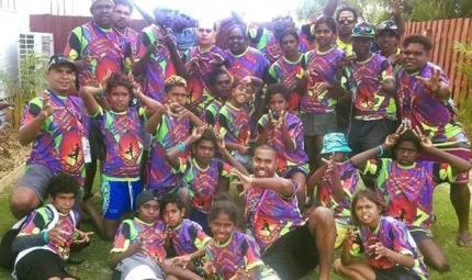 Aboriginal adults and youth in colourful shirts sitting on grass.