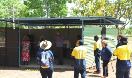 Group of Indigenous and non-Indigenous people standing in and outside of a green shed with a cross on top.