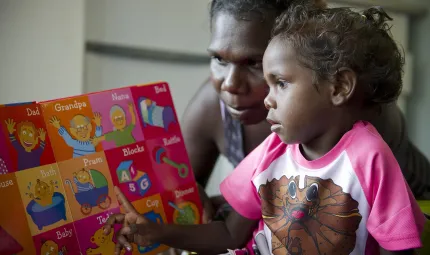 Aboriginal woman and young girl read a colourful child’s picture book together.