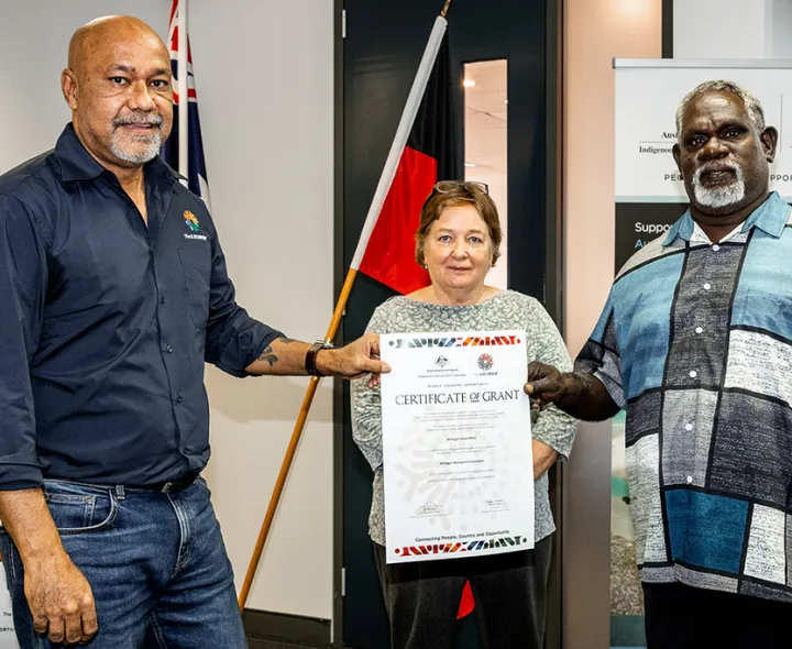 Two men hold a Certificate up in front of a woman in an office