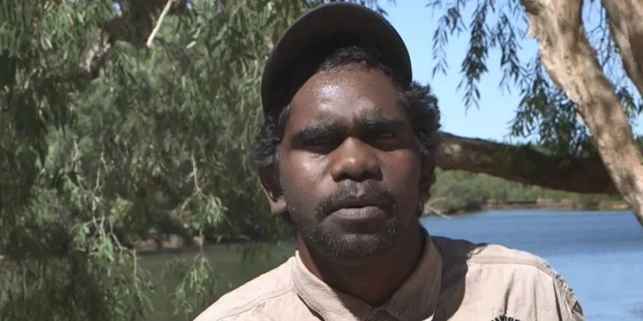 Aboriginal young man dressed in ranger uniform in foreground with river and trees in the background.