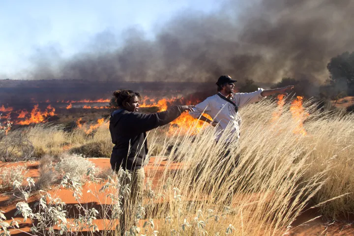 Female ranger and male ranger standing in desert setting with burning grass in the background.