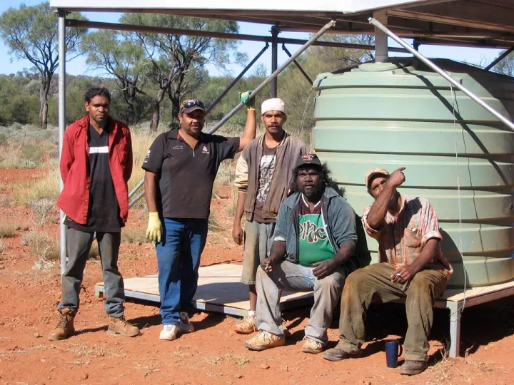 Five Indigenous men in front of a water tank