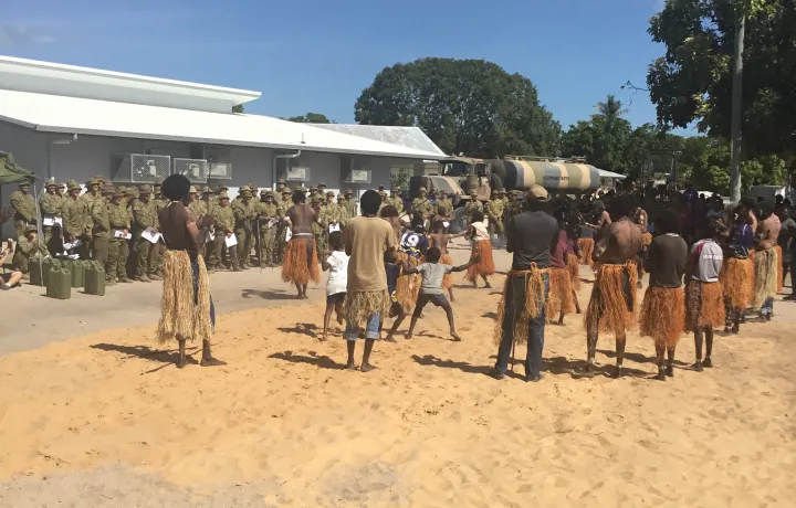 A group of dancers in grass skirts dancing on sand for a group of army soldiers wearing green fatigues.