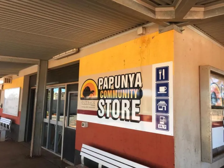 We see the corner of a shop and the eaves at the top. At the shopfront are two silver coloured benches. There are various signs on the walls including the words: Panunya Community Store.