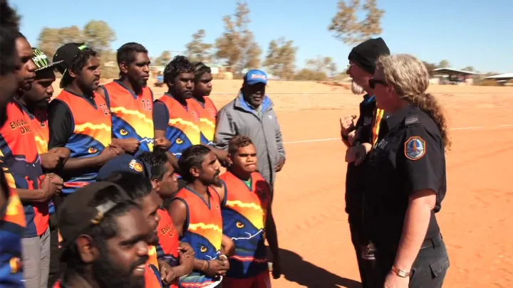 Group of Aboriginal footballers and others associated with the team on an ochre coloured football field.