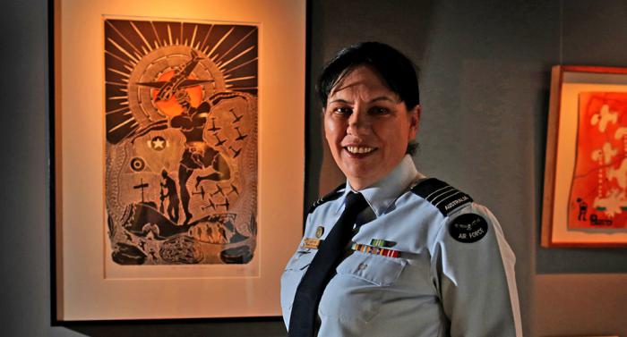 Wing Commander Cheryl Neal dressed in her air force uniform is standing in front of Indigenous artwork.