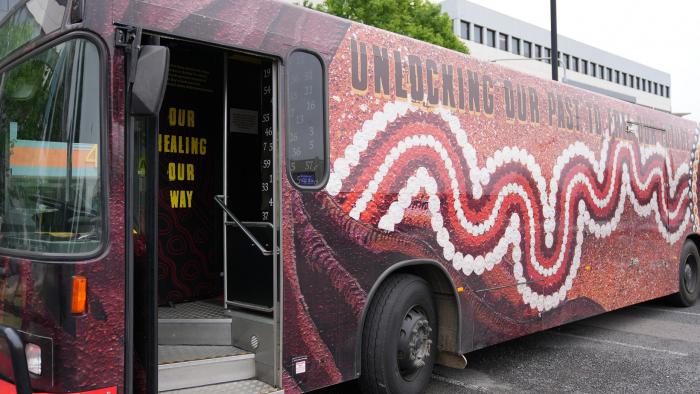Image of a bus parked outside an office. It is painted with an Indigenous style design.