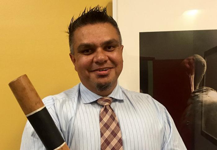 Aboriginal man dressed in shirt and tie and holding a didgeridoo.