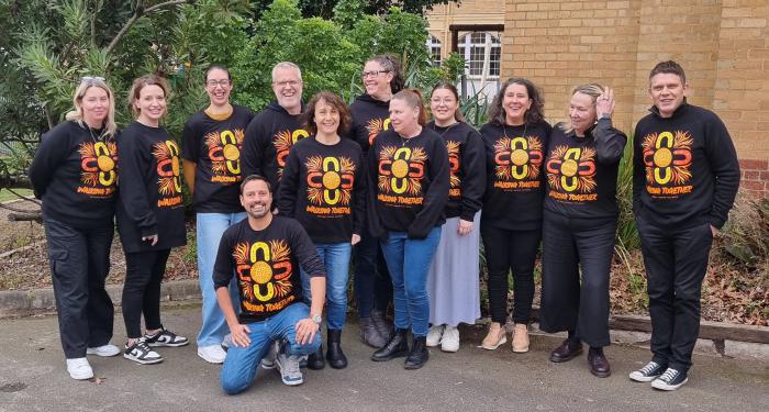 A group of smiling people wearing shirts with a matching brightly coloured design and the text 'Walking Together'